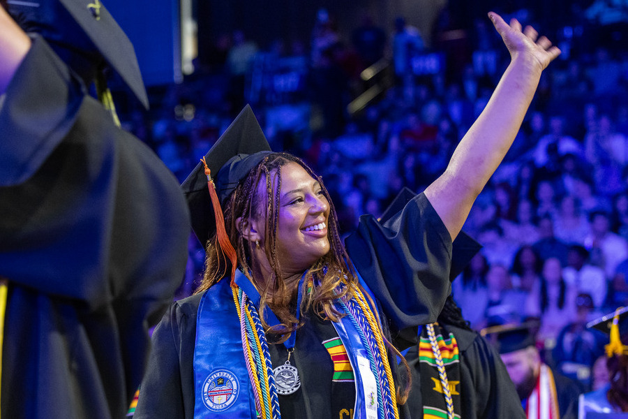 A happy graduate in a cap and gown waves at commencement 2026.