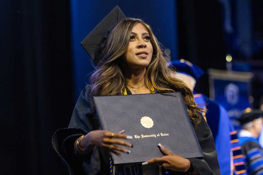 University of Tulsa graduate in cap and gown holding diploma at commencement 2026.