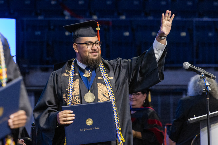 Graduate waves at commencement 2026, holding diploma