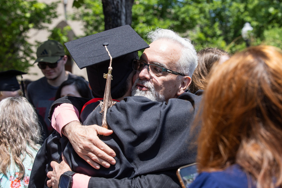 Graduate commencement 2026: A guest hugs a graduate in a black cap and gown.