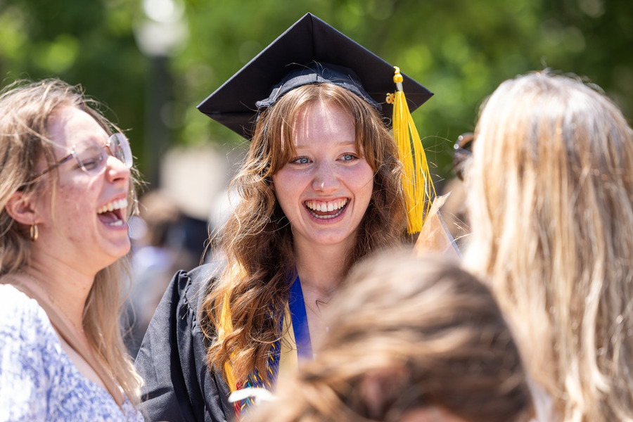 Graduate in cap and gown smiles with friends at commencement 2026.