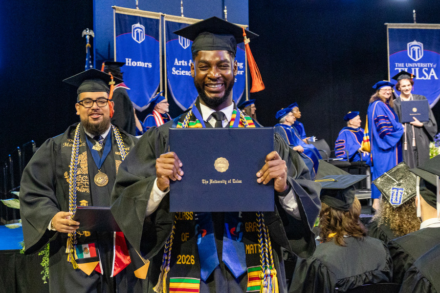 Graduate commencement 2026: Smiling graduate holds diploma at University of Tulsa ceremony.