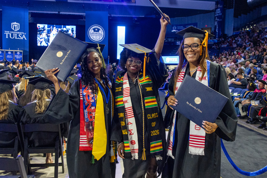 Three graduates in caps and gowns at commencement 2026, holding diplomas.