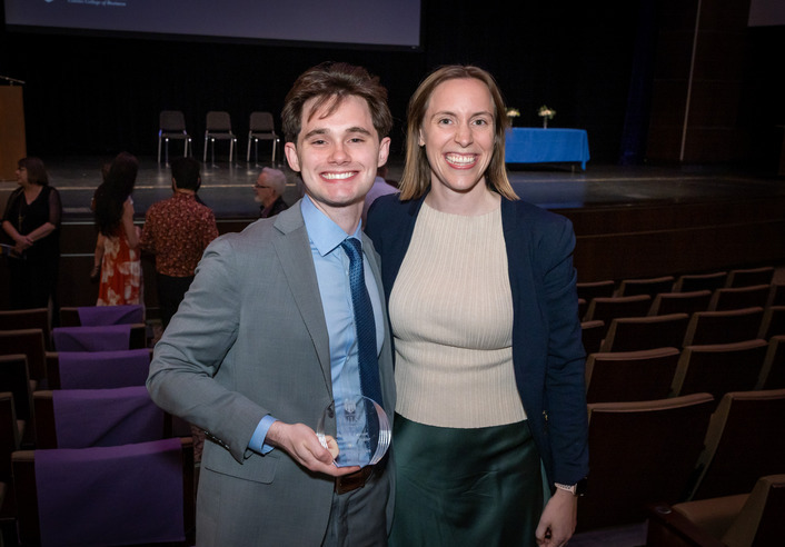 Young man in a suit accepts award with a woman at an event