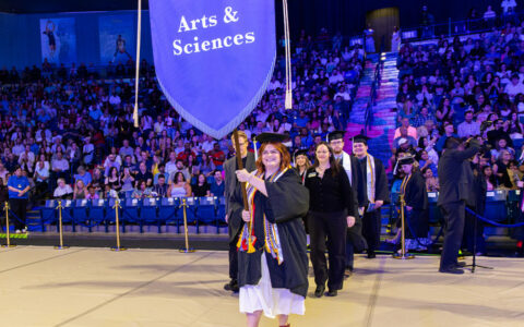 Kadee Jo Ransom, A&S Honor Marshal, leads 2026 graduates with Arts & Sciences banner.