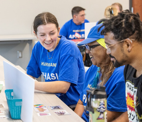 UTulsa students in blue shirts at at an Aphasia workshop, smiling and interacting.