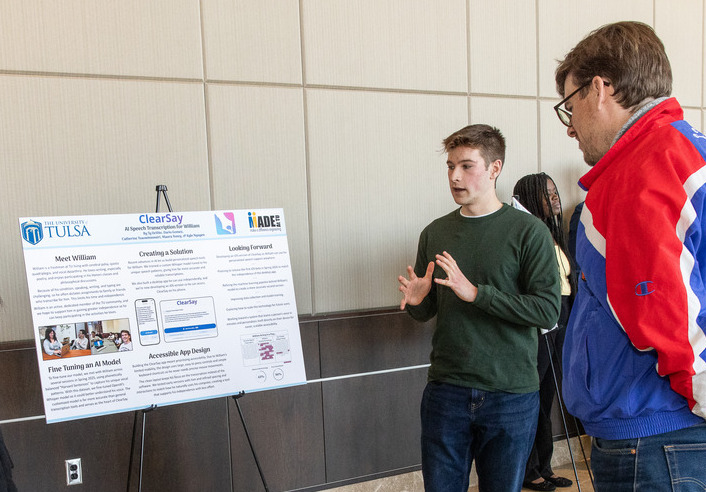 Student presents ClearSay AI project poster to man at The University of Tulsa