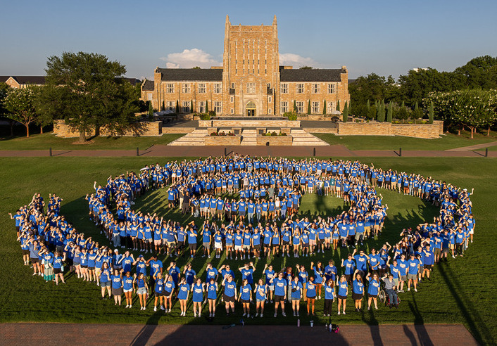 Group of students in blue shirts forming a hurricane shape in front of McFarlin Library