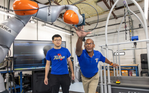 Professor reaches for robot arm in lab while student watches