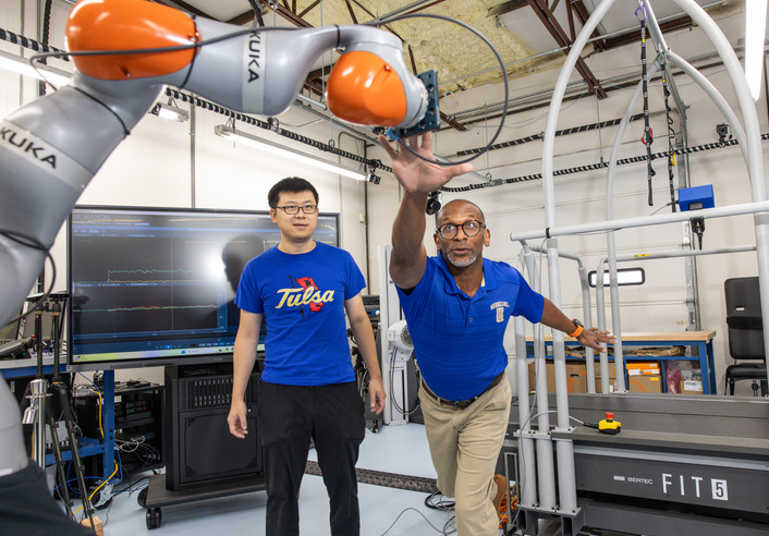 Professor reaches for robot arm in lab while student watches