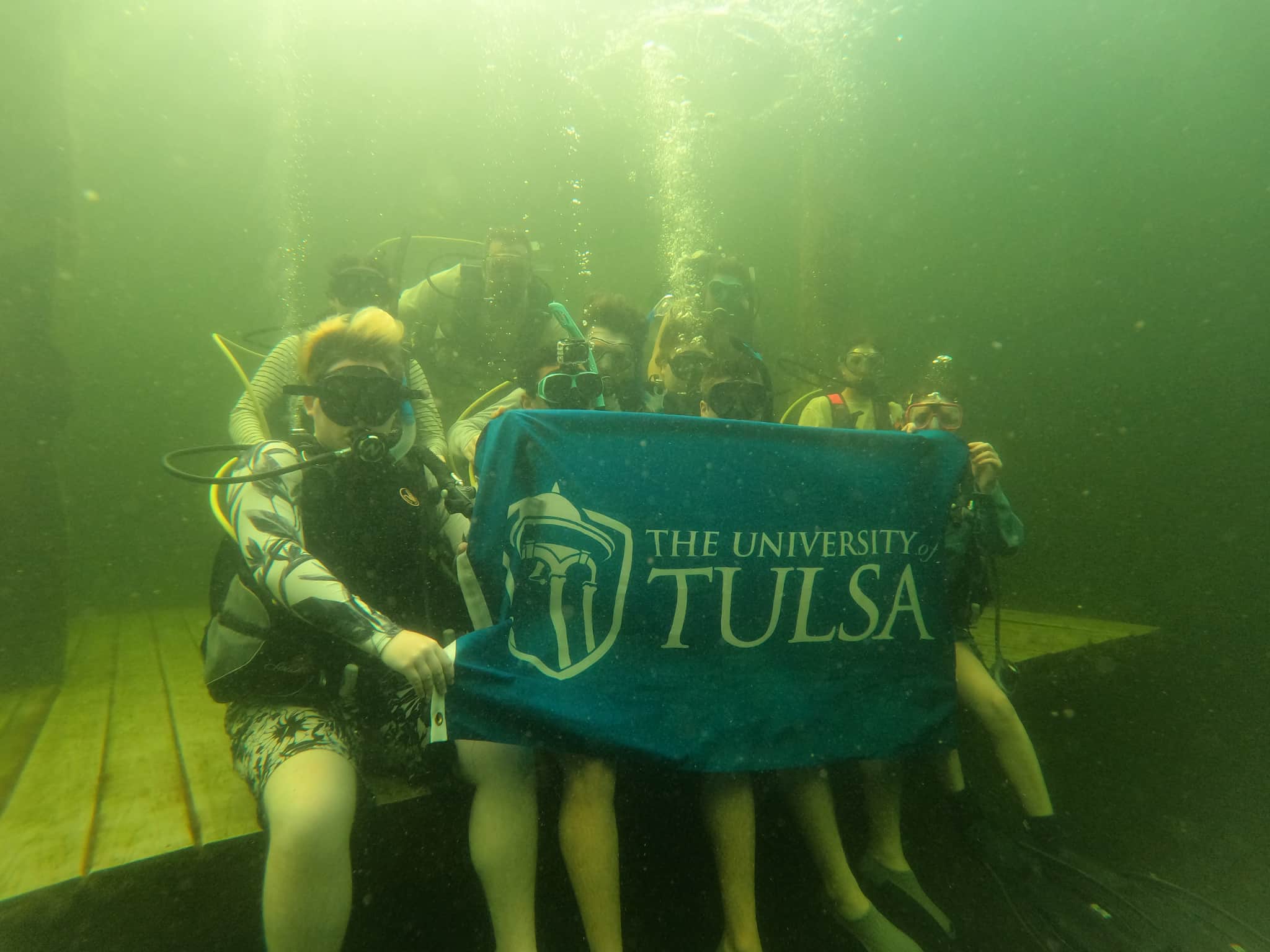 Scuba divers hold University of Tulsa flag underwater