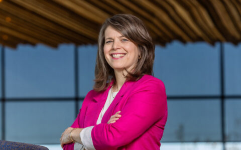 Rachel Gold in pink blazer, arms crossed