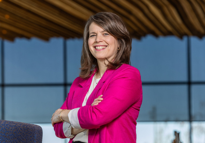 Rachel Gold in pink blazer, arms crossed