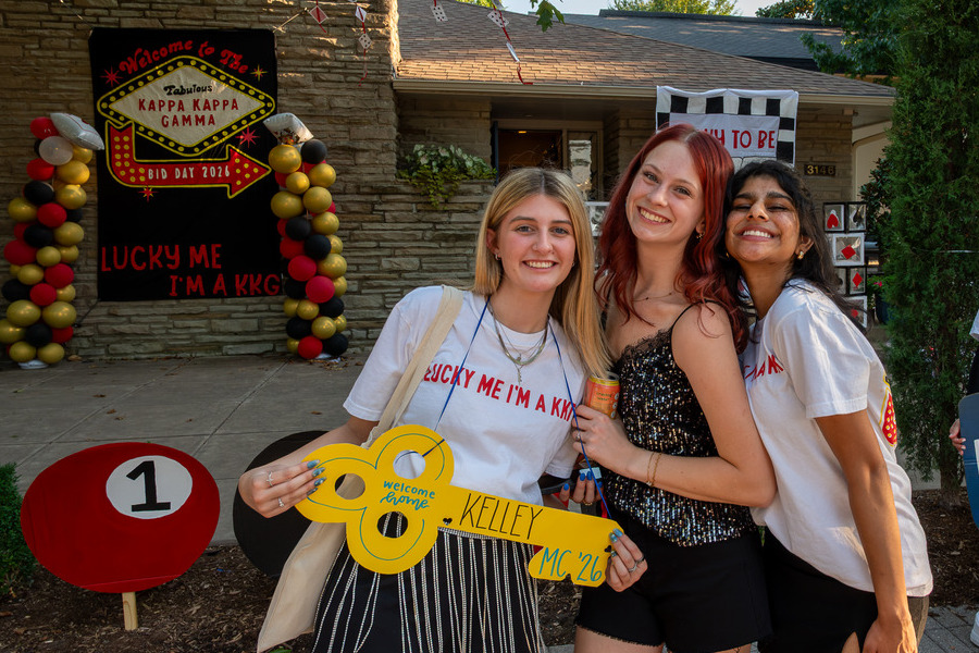 Three smiling women pose outside Kappa Kappa Gamma house, decorated in a Las Vegas theme