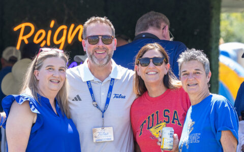 Four people in Tulsa gear smiling at the football tailgate