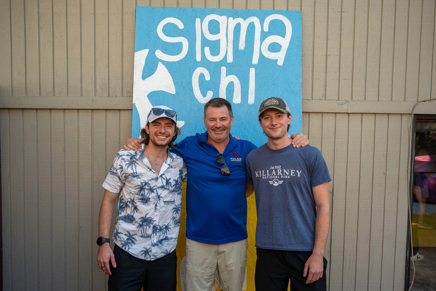 Three men pose in front of Sigma Chi sign