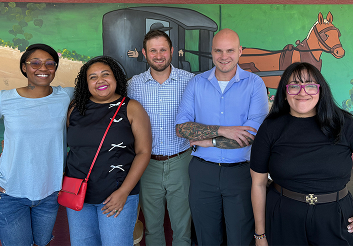 Five people pose in front of mural